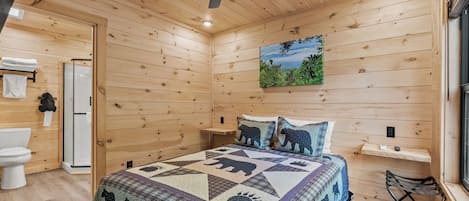 A wooden cabin bedroom with a bed, a ceiling fan, a shower, and a painting on the wall.
