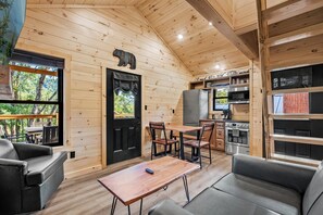 A cabin interior with a dining area, kitchen, and a large window overlooking a deck.