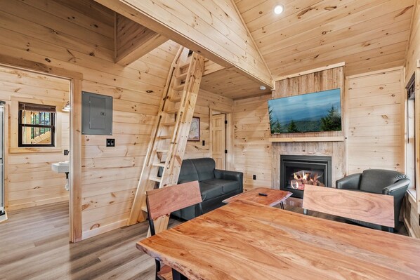 A wooden cabin interior with a fireplace, a sofa, a dining table, and a ladder. - TreeLodge, Downtown Pigeon Forge (Pigeon Forge)