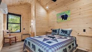 Een slaapkamer in een houten blokhut met een bed, een raam, een stoel en een plafondventilator.