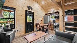 Een blokhutinterieur met een eethoek, keuken en een groot raam met uitzicht op een bos.