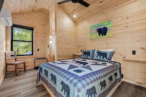 A wooden cabin bedroom with a bed, a window, a chair, and a ceiling fan. - TreeLodge, Downtown Pigeon Forge (Pigeon Forge)