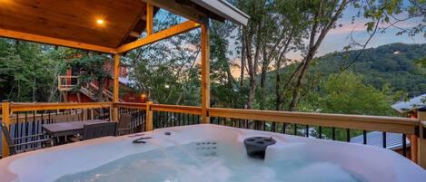 A hot tub on a wooden deck with a view of trees and hills.