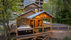 A wooden cabin with a deck, a hot tub, and a covered seating area.