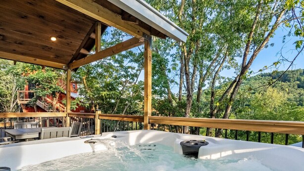 Een hottub met een houten terras en buiten zitplaatsen, omringd door bomen en uitzicht op een bebost gebied.