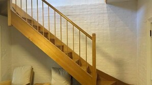 A wooden staircase with a white brick wall and a sofa with cushions. - Urban Nook Serviced Apartments (Launceston)