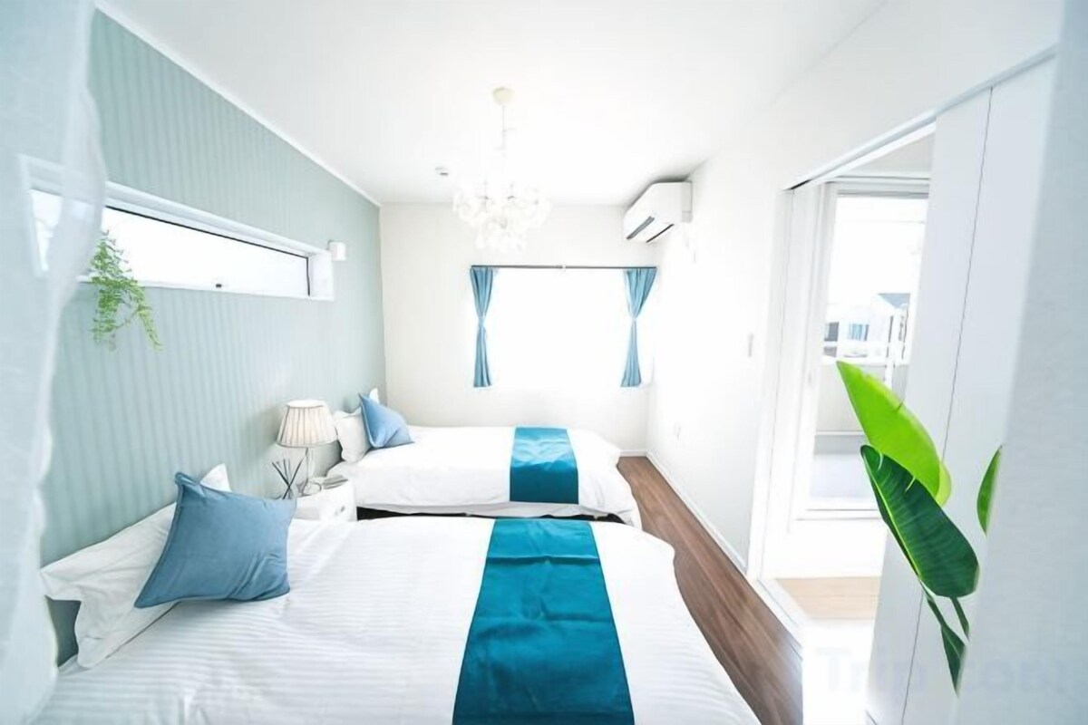 A modern bedroom with two beds, a chandelier, and a large window with curtains.