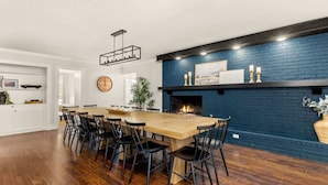 Un comedor con mesa y sillas de madera, una chimenea de ladrillo azul y un reloj en la pared.