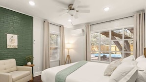 Un dormitorio con cama, una silla, ventilador de techo, ventana con cortinas y aire acondicionado instalado en la pared.