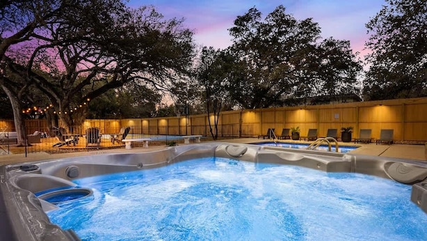 Zona de hidromasaje con asientos y piscina, rodeada de árboles y una valla.