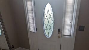Une pièce dotée d’un sol carrelé, d’une porte blanche ornée d’une fenêtre à motifs losangés et d’un miroir appuyé contre le mur.