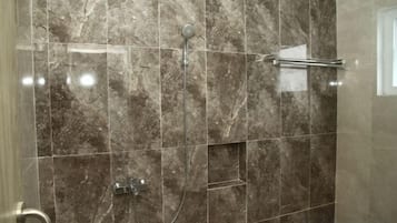 Un bagno con una parete in marmo, una doccia con soffione manuale e un portasciugamani.