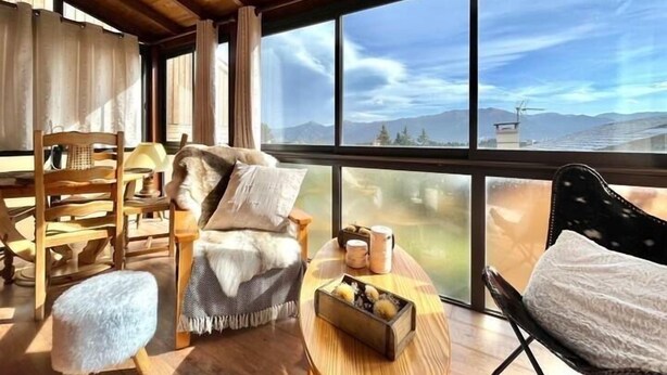 A cozy room with a large window, wooden furniture, and a view of mountains.