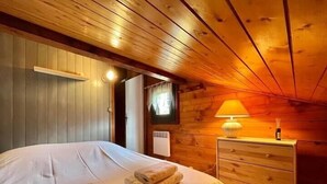 A cozy wooden room with a bed, a dresser, and a lamp.
