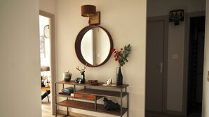 Un pasillo con una consola de madera, un espejo redondo y un florero con flores.