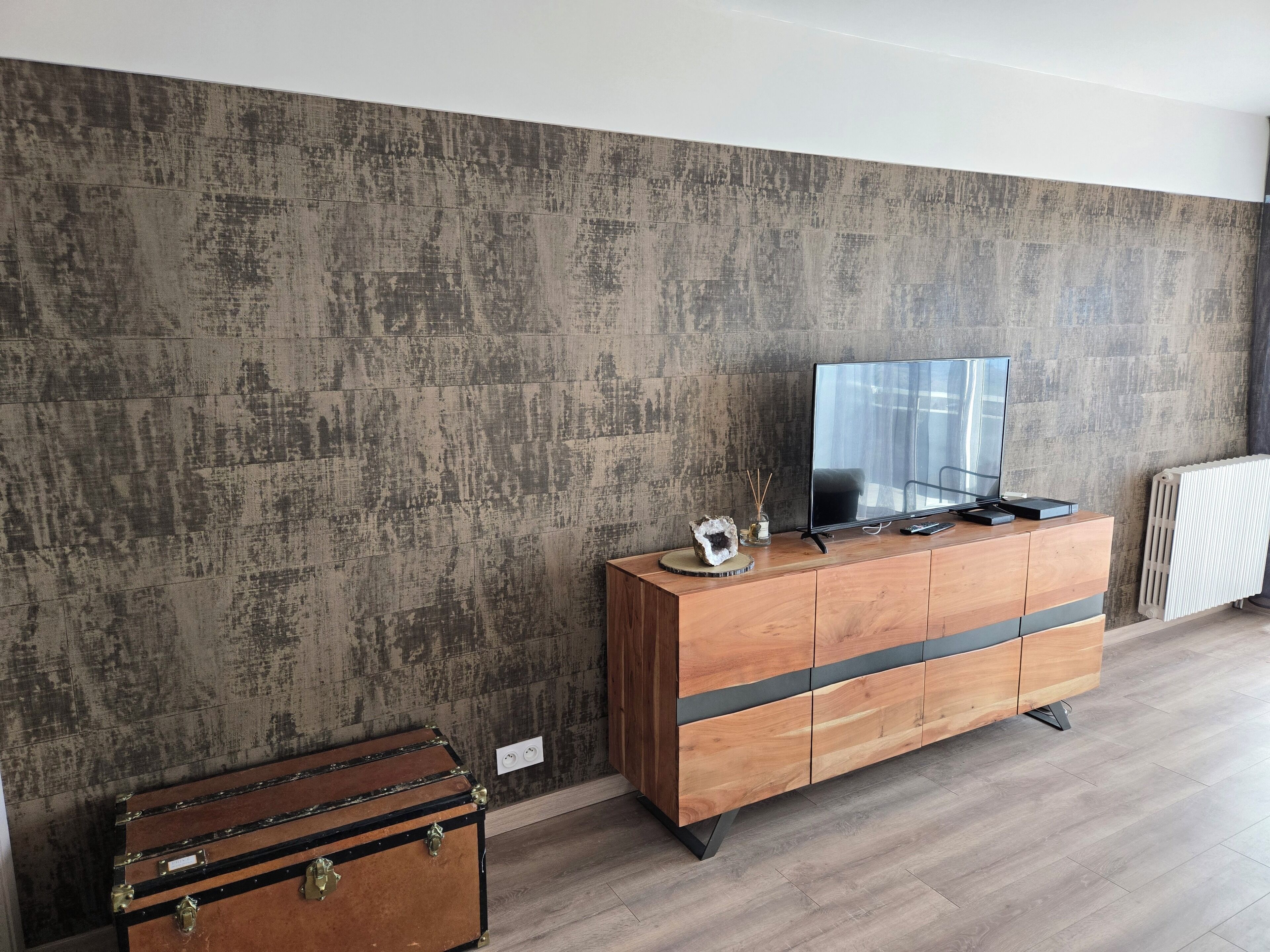 A modern living room with a wooden cabinet, a flat-screen TV, and a vintage suitcase.