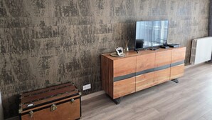 Una sala de estar moderna con un aparador de madera, un televisor de pantalla plana y una maleta antigua.