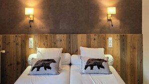 Cama doble con dos almohadas, cabecera de madera y dos luces fijadas a la pared.