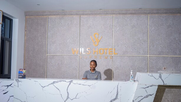 A reception desk at WIL'S HOTEL SUPREME with a marble top and a logo above the name. - Wils Hotel SUpreme (Lusaka)