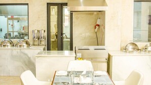 A modern dining area with a marble countertop, a central table with four chairs, and a kitchen in the background. - Wils Hotel SUpreme (Lusaka)