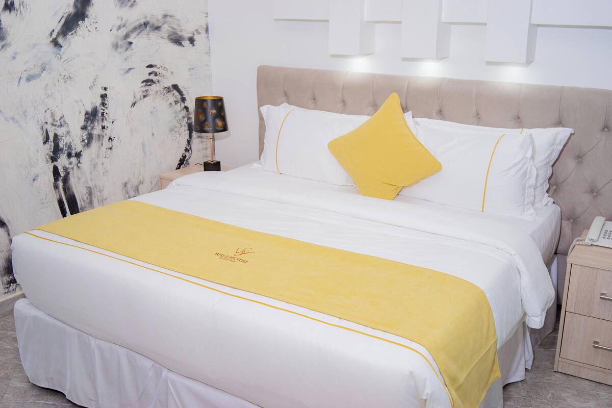 A hotel room with a large bed, a bedside table, and a wall with abstract art.