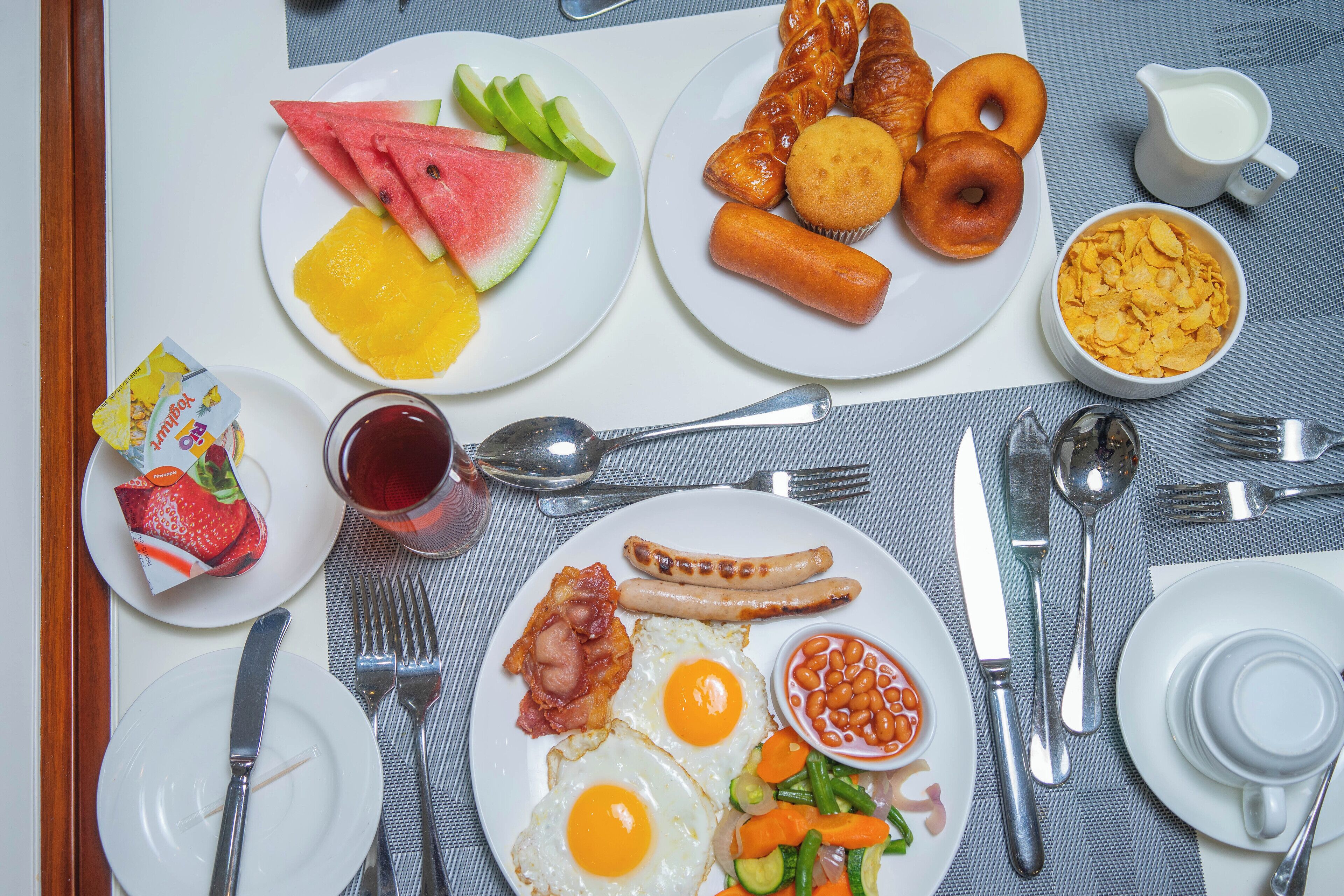 Un assortiment de plats variés pour le petit-déjeuner, comprenant des œufs, des saucisses et des fruits.
