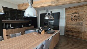 A modern kitchen with a wooden island, black cabinets, and a rustic wooden wall. - Loft Eclipse 1723 (Font-Romeu-Odeillo-Via)