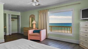 Une chambre avec un grand lit, une chaise, une commode, un miroir et une vue sur la plage.