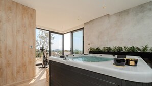 A modern spa area with a large hot tub, wooden flooring, and a view of the outdoors.