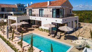 A modern two-story house with a swimming pool, outdoor seating, and a view of the surrounding landscape.