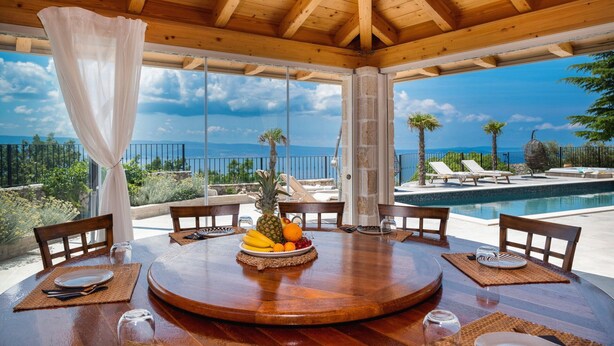 A wooden dining area with a view of a pool and ocean. - Villa La Rustica with Pool (Jesenice)
