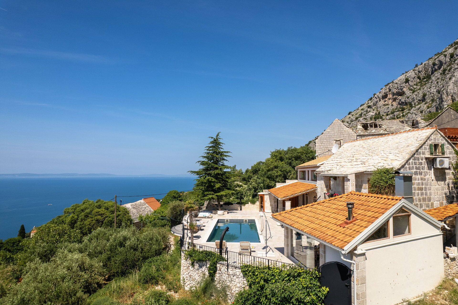 A coastal villa with a swimming pool, stone walls, and a view of the sea.