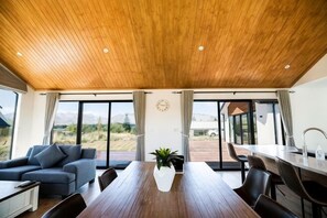 A modern dining area with a wooden ceiling, large windows, and a view of the outdoors. - RodmanStar Apartment (Lake Tekapo)