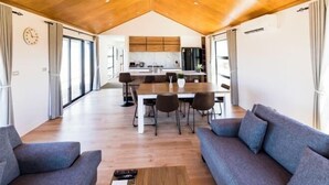A spacious living area with a wooden ceiling, a dining table with chairs, a sofa, and a kitchen in the background. - RodmanStar Apartment (Lake Tekapo)