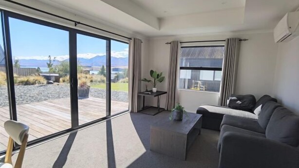 A modern living room with a large sliding glass door, a sofa, a coffee table, and a small side table with a plant. - RodmanStar Apartment (Lake Tekapo)