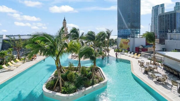 Una piscina en la azotea con palmeras, sillones de descanso y vistas del horizonte de la ciudad.