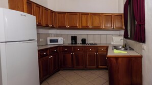 Eine kleine Küche mit Holzausstattung, einem weißen Kühlschrank, einer Mikrowelle, einer Kaffeemaschine und einem Spülbecken.
