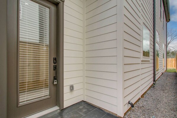 Fachada de casa con puerta principal, buzón y pequeño jardín delantero con grava.