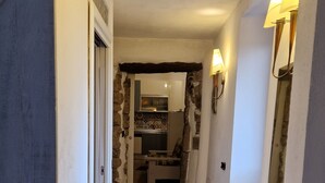 Un couloir au plancher en bois mène à une cuisine dont le mur derrière l’évier est recouvert de carreaux.