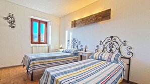 Une chambre avec deux lits, une fenêtre, un radiateur, une table de chevet et un luminaire fixé au mur.