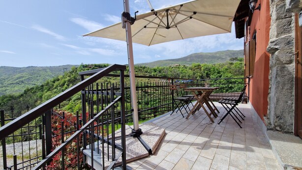 Un balcon avec une table et des chaises, un grand parasol et une vue sur un paysage montagneux.