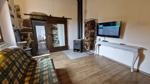 Un salon chaleureux avec un canapé à carreaux, une cheminée, un téléviseur fixé au mur et un mur en pierre rustique.