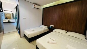 Une chambre d’hôtel avec deux lits, une tête de lit en bois, une petite table de chevet et une salle de bain visible à travers une porte ouverte.