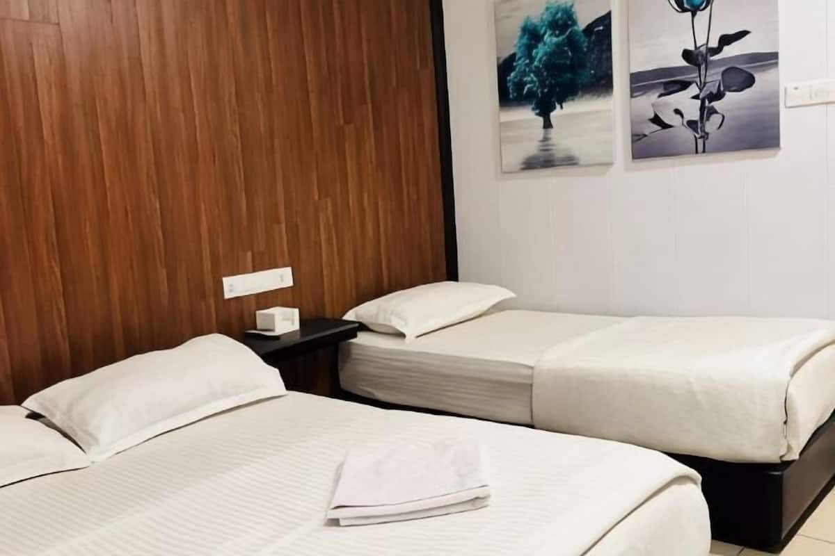 A hotel room with two beds, wooden headboard, white bedding, and a nightstand with a lamp.