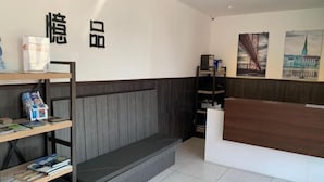 Un espace d’accueil comprenant un comptoir en bois, un banc et une bibliothèque avec des magazines.