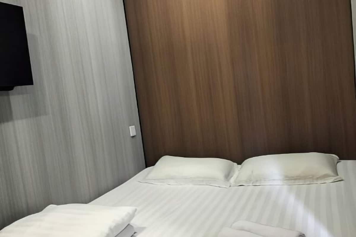 A neatly made bed with white linens and pillows, a wooden headboard, and a wall-mounted television.