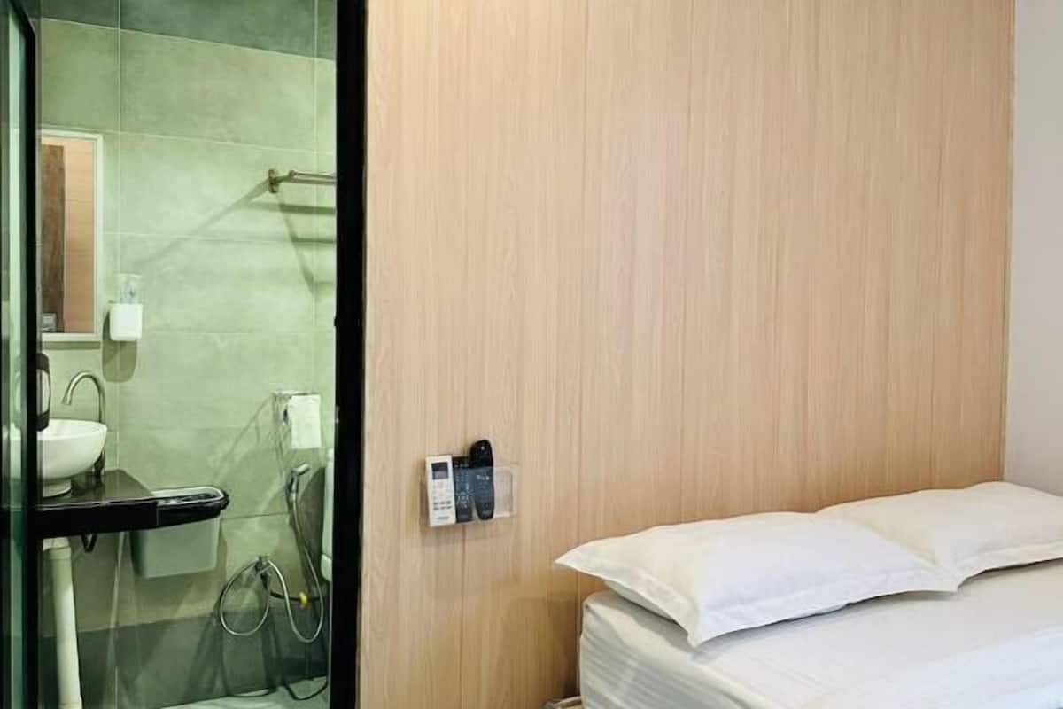 A hotel room with a wooden wall, a bed with white bedding, a bathroom with a sink and mirror, and a telephone.