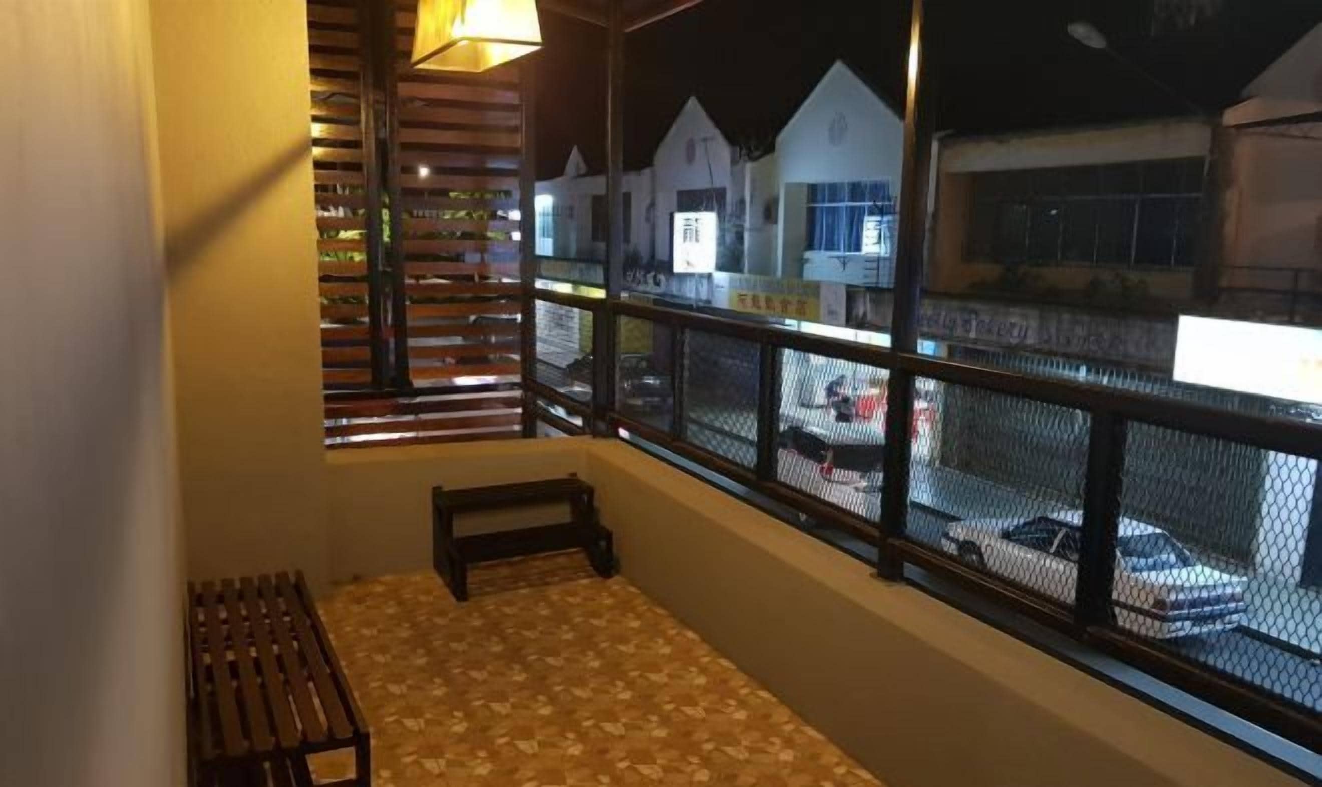 A balcony with a wooden bench, a railing, and a view of a street with buildings and parked cars.