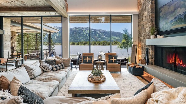 Ein geräumiges Wohnzimmer mit großem Fenster mit Blick auf einen See und Berge, inklusive Kamin und gemütlicher Sitzecke.