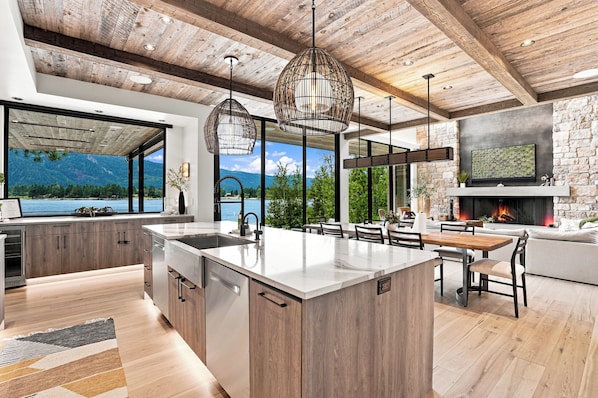 Une cuisine moderne dotée d’un grand îlot central, de poutres en bois au plafond et offrant une vue sur les montagnes.